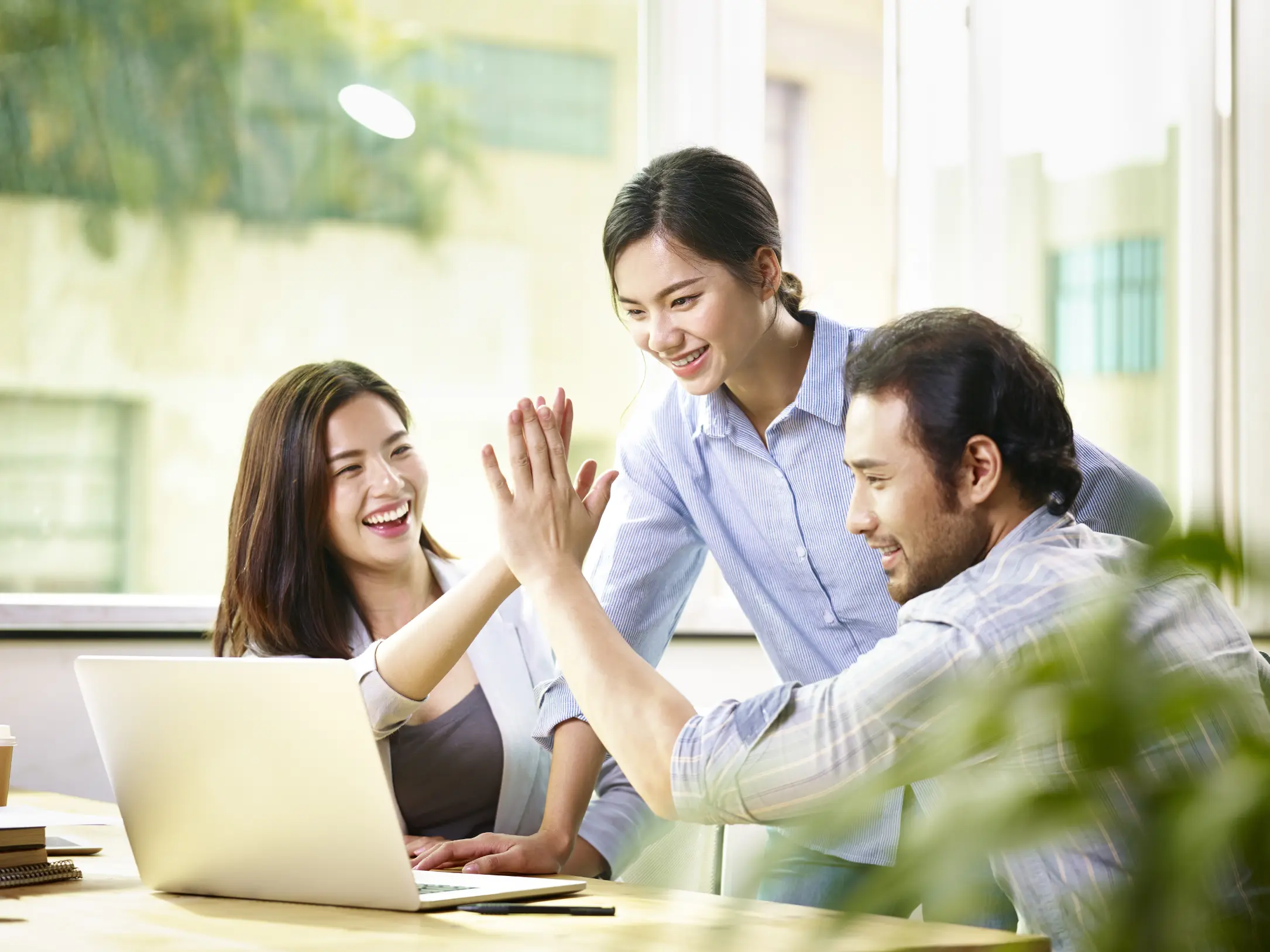 Team celebrating a successful financial strategy with a high-five while reviewing results on a laptop