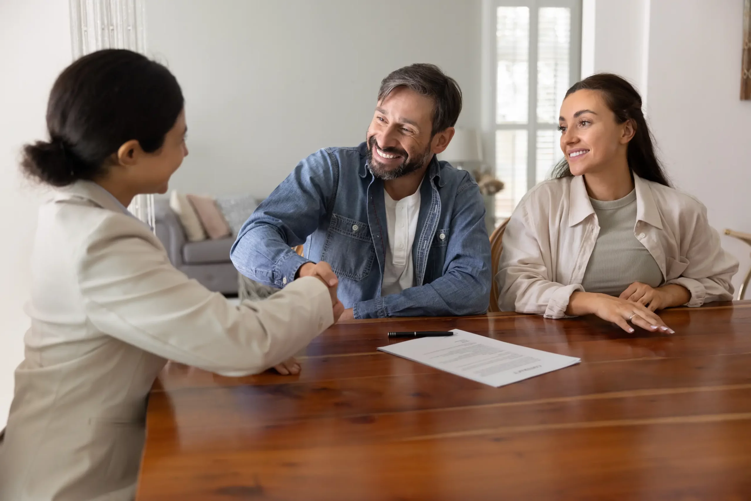 Business consultant shaking hands with a client while a colleague observes during a financial advisory meeting