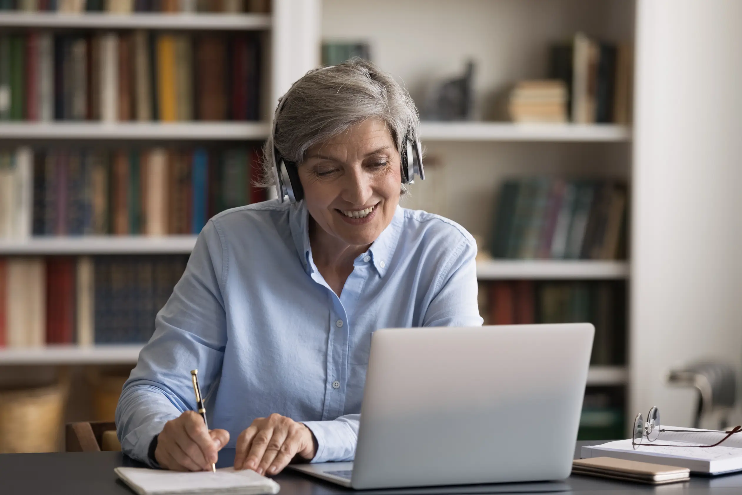 Senior woman wearing a headset working on a laptop while reviewing tax strategy and insurance planning details
